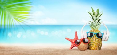 Yaz tropikal denizi, köpüklü dalgalar, ananas ve hindistan cevizi güneş gözlüğü ve kulaklıkla sıcak kumsalda. Kopya alanı ile seyahat ve tatil kavramı
