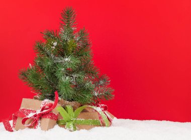 Kırmızı arkaplan önünde küçük köknar ağacı ve hediye kutuları olan Noel tebrik kartı ve yılbaşı kutlamalarınız için yer kopyalama