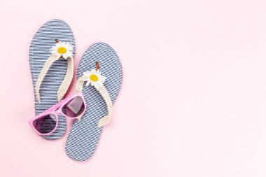 Çiçekli plaj terlikleri ve pembe arka planda güneş gözlükleri. Yaz tatili kavramı. Kopyalama alanı olan düz
