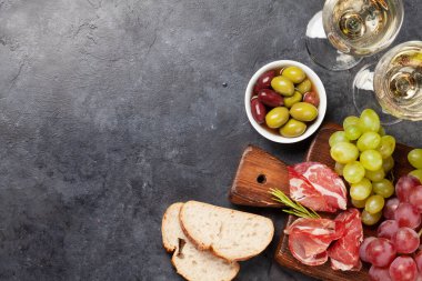 Prosciutto, zeytin ve üzümlü Antipasto tabağı. Aperatif panosu ve beyaz şarap. Üst görünüm düzlüğü kopyalama alanı ile yatıyordu