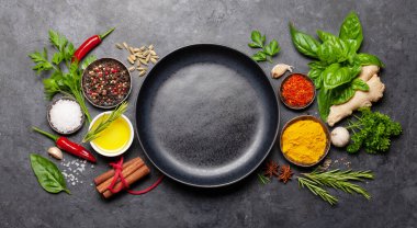 Koyu taş masadaki çeşitli baharatlar, otlar ve baharatlar. Hint mutfağı. Üst görünüm düz, boş tabakla yatıyordu