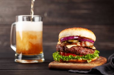 Büyük sığır eti, peynir, domates, pastırma, marul ve bira bardağıyla ev yapımı lezzetli hamburger. Kopyalama alanı ile