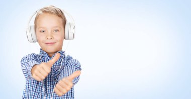 Kulaklıkla müzik dinleyen ve baş parmak kaldıran genç bir çocuk. Kopyalama alanı olan mavi arkaplan