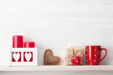 Sevgililer Günü kutlaması. Kahve fincanı, hediye kutusu ve rafta mumlar. Ahşap duvarın önünde.