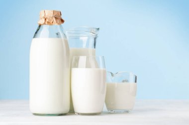 Şişede süt, sürahi, bardak ve bardak. Mavi arkaplanın önünde. Kopyalama alanı ile