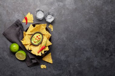 Meksika cipsi, guacamole sosu ve tekila shot 'ı. Üst görünüm düz taş masa üzerinde kopya alanı ile yatıyordu
