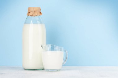 Şişede süt ve cam sürahi. Mavi arkaplanın önünde. Kopyalama alanı ile