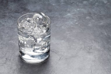 Taş masanın üzerinde buz küpleri olan bir bardak su. Kopyalama alanı ile