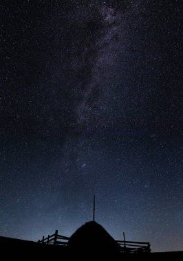 Gece gökyüzünde yıldızlar ve görünür Samanyolu ile karşı saman yığını silüeti