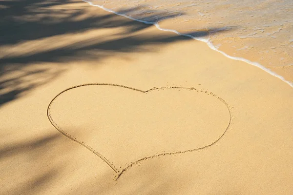 Сердце на песчаном пляже с пальмовой тенью и морской волной — стоковое фото