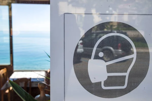 Карантинный знак "обязательно носить маску внутри" на двери ресторана в Сицилии, Италия — стоковое фото