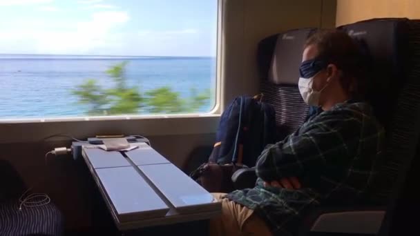 Неопознанный человек в маске для сна и защитной медицинской маске спит в поезде — стоковое видео
