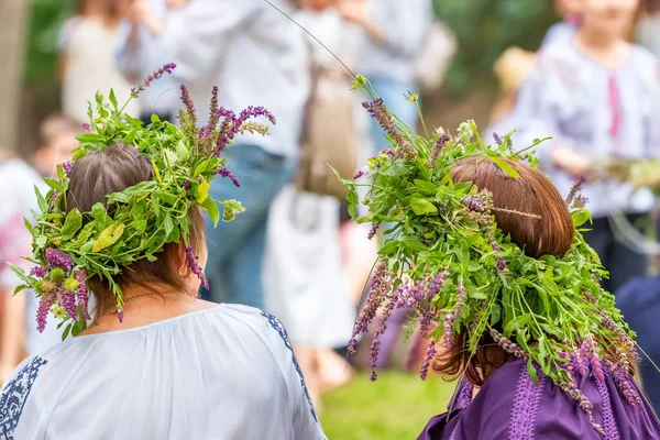Tarla çiçekleri, çimenler ve tahıllardan yapılmış yaz gündönümü çelenkleriyle geleneksel elbiseli tanımlanamayan kadınlar.. — Stok fotoğraf