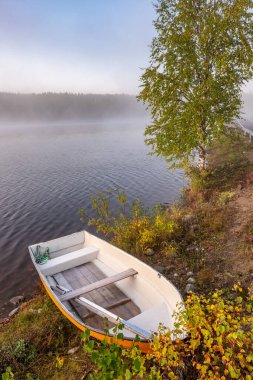 Finlandiya 'da sonbaharda göl kıyısında küçük tahta bir tekne.