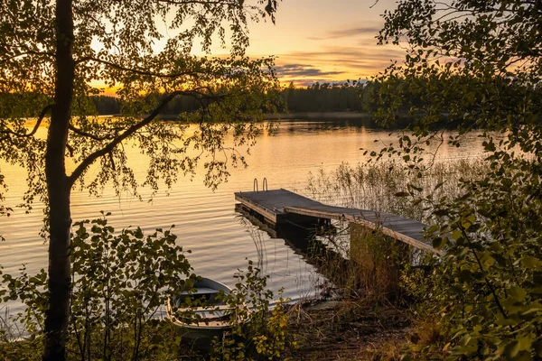Ξύλινη προβλήτα και μικρό σκάφος σε μια ήρεμη λίμνη στο ηλιοβασίλεμα στη Φινλανδία — Φωτογραφία Αρχείου