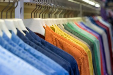 Butik dükkanında askıda asılı parlak renkli pamuklu gömlekler. Kapatın.