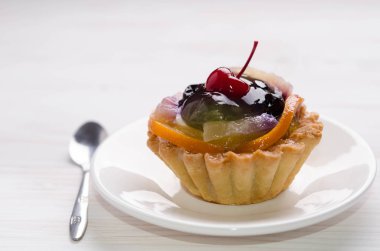 Beyaz masada farklı meyvelerle süslenmiş sepet kek.