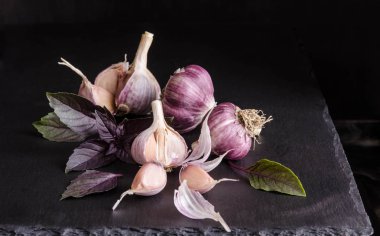 Siyah arka plan üzerine siyah taş masada sarımsak ve fesleğen yaprakları