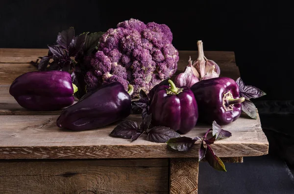新鲜蔬菜深紫色的辣椒 花椰菜与罗勒和大蒜的叶子在老质朴的木桌上黑色背景 — 图库照片