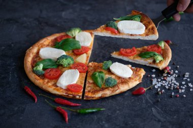 Pizza Mozzarella peyniri, domates, brokoli, baharat ve taze fesleğen ile dilimlenmiş. İtalyan pizza. Siyah taş zemin üzerine pizza