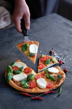 Pizza Mozzarella peyniri, domates, brokoli, baharat ve taze fesleğen ile dilimlenmiş. İtalyan pizza. Siyah taş zemin üzerine pizza