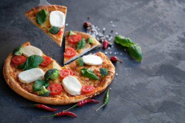 Pizza Mozzarella peyniri, domates, brokoli, baharat ve taze fesleğen ile dilimlenmiş. İtalyan pizza. Siyah taş adam pizzaya