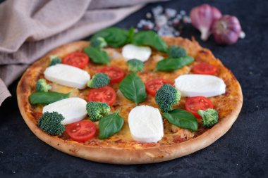 İtalyan pizza Mozzarella peyniri, domates, brokoli, baharat ve taze fesleğen. Siyah taş zemin üzerine yakınındaki, pizza ve mutfak peçete