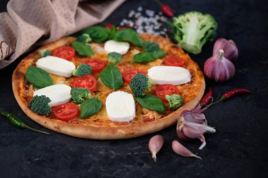 İtalyan pizza Mozzarella peyniri, domates, brokoli, baharat ve taze fesleğen. Siyah taş zemin üzerine yakınındaki, pizza ve mutfak peçete