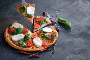 Pizza Mozzarella peyniri, domates, brokoli, baharat ve taze fesleğen ile dilimlenmiş. İtalyan pizza. Siyah taş zemin üzerine pizza