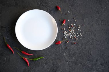 Siyah taş zemin üzerine beyaz tabak. Sıcak biber biber, tuz bir