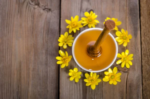 Honey in the glass bowl, dipper and yellow flowers around it on — Stock Photo, Image