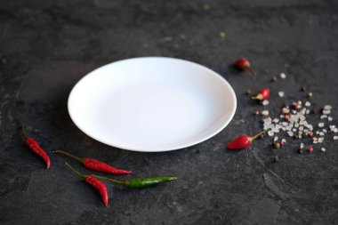 Siyah taş arka planda beyaz plaka. Sıcak biberli biber, tuz 