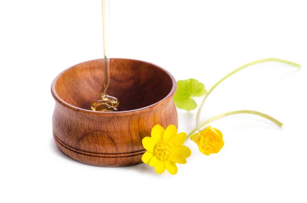 Pouring honey in the wooden bowl with yellow flowers isolated on — Stock Photo, Image