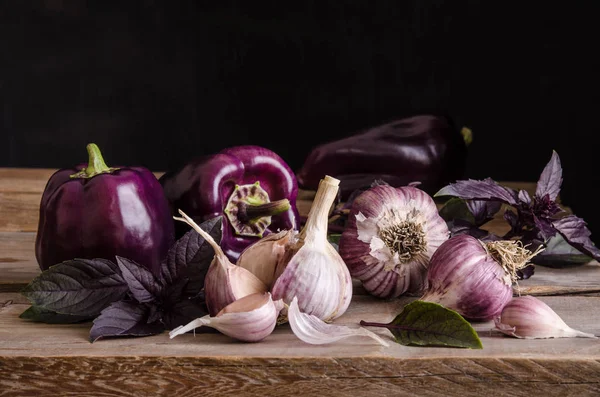 Dark purple peppers with leaves of basil and garlic — Stock Photo, Image