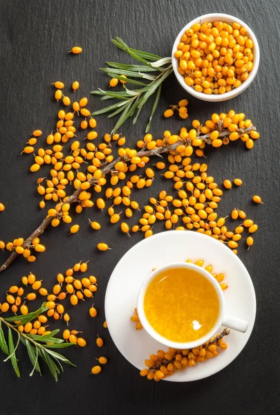 Sea buckthorn and cup of  tea on black stone table. — Stock Photo, Image