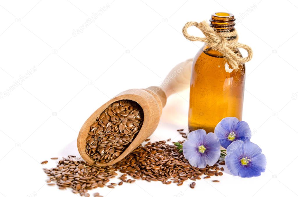 Flax seeds in the wooden scoop, bottle with oil and flowers