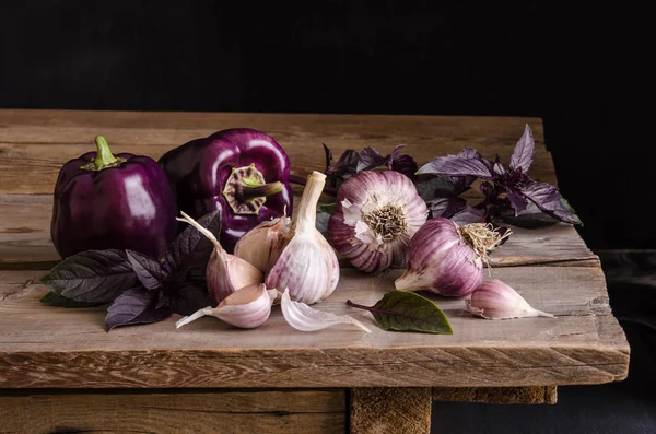Dark purple peppers with leaves of basil and garlic — Stock Photo, Image
