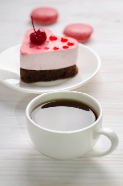 kalp şeklinde sufle keki, bir fincan kahve ve ahşap bir masada badem kurabiyesi.