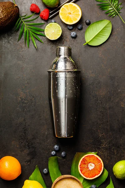 Coctelera, frutas tropicales y hojas sobre un fondo oscuro —  Fotos de Stock