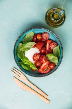 Caprese salatası. Mozzarella peyniri, domates ve fesleğen bitki yaprakları. Mavi arka plan. Üstten görünüm