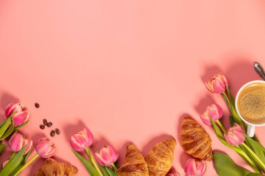 Sabah kahvesi, kruvasan ve pembe arka planda güzel bir çiçek. Sıcak kahvaltı çerçevesi. Blogcular, dergiler, web tasarımcıları, sosyal medya ve sanatçılar için düz konum.