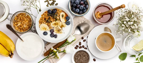 Zab granola, joghurt, méz, friss banán, áfonya, chia mag tálba, és kávét a fehér háttér — Stock Fotó