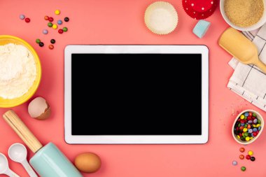 Pembe arka plan üzerinde boş tablet ile pişirme malzemeleri, düz yatıyordu
