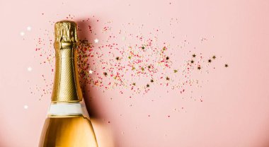Flat lay of Celebration. Champagne bottle with sprinkles on pink background. clipart