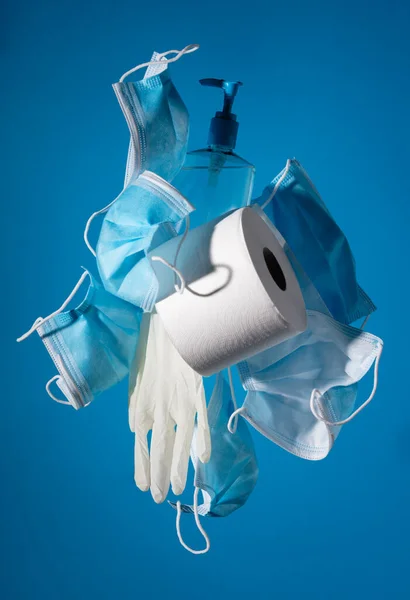 Flygande masker, handskar, toalettpapper och rengöringsmedel på blå bakgrund. En vy av en grundläggande Covid 19 kit. — Stockfoto