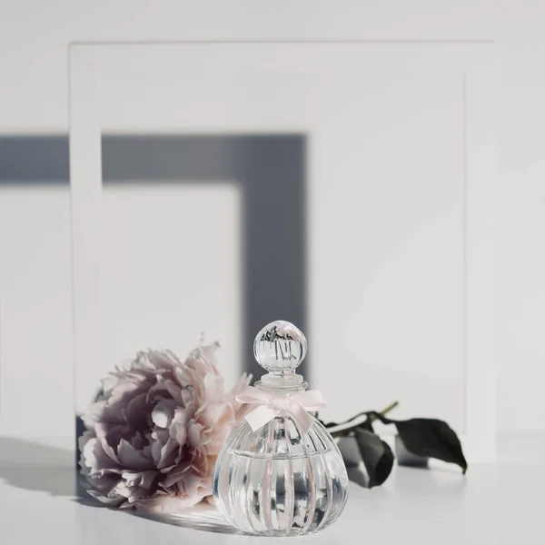 Flor peopy rosa, frasco de perfume y marco de madera blanco contra pared blanca — Foto de Stock