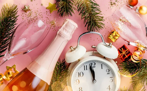 Natale o Capodanno composizione su sfondo rosa con sveglia retrò, bottiglia di champagne, bicchieri e decorazioni natalizie — Foto Stock