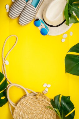 Hasır şapka, kamera, çanta, yaz ayakkabıları, güneş gözlükleri, kabuklar ve sarı arka planda tropikal yapraklar.