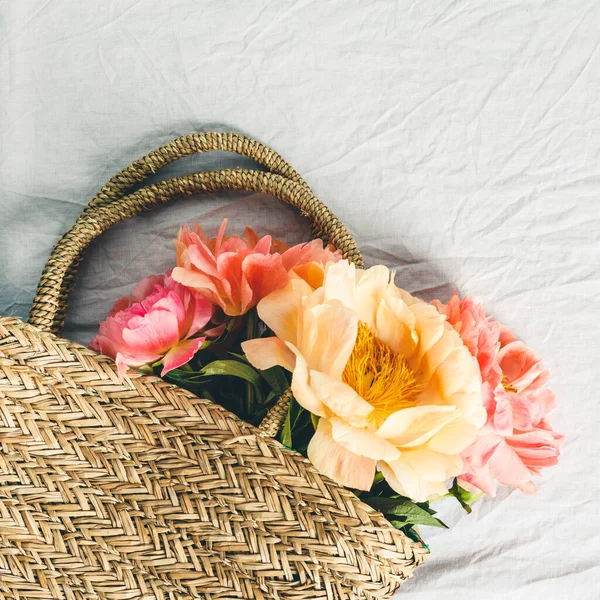 Flat-lay de hermosas flores de peonía en bolsa de paja sobre fondo de mantel de lino gris — Foto de Stock