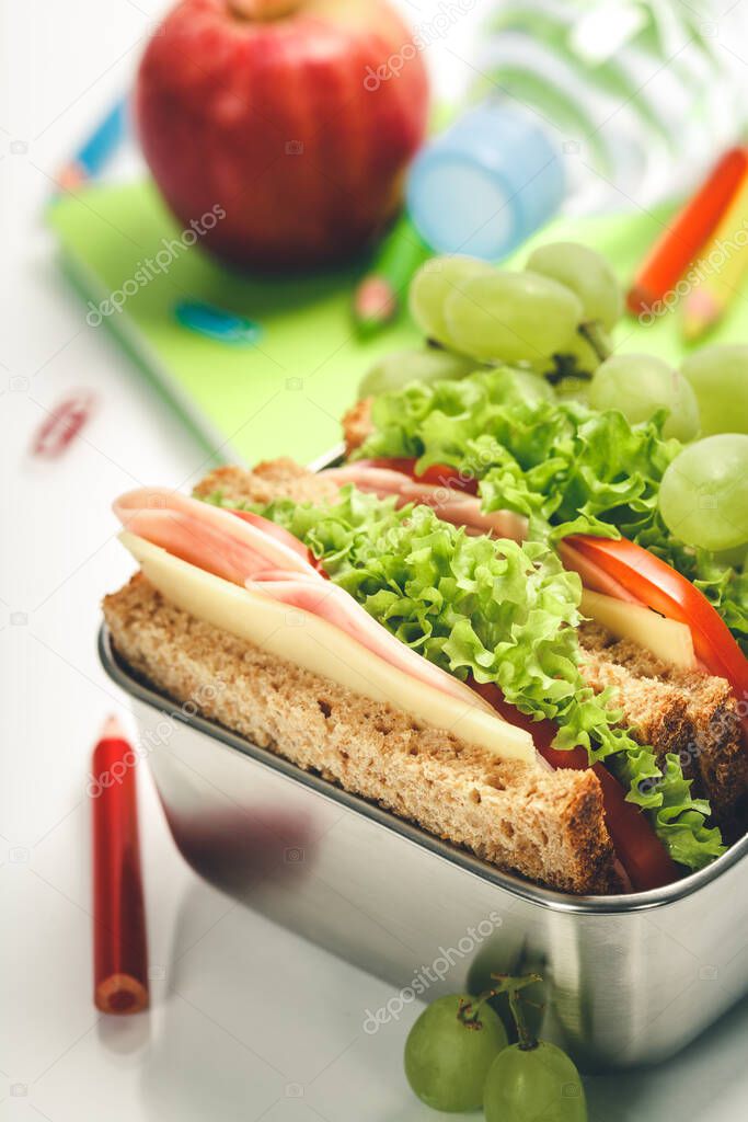 Lunch box with sandwich and fruits, school notebooks, stationery on white background